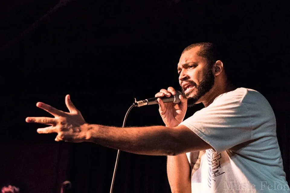 EyeQ performing with an outstretched arm under stage lights.